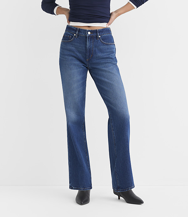 A person wearing blue flared jeans and black heeled boots stands against a plain white background.