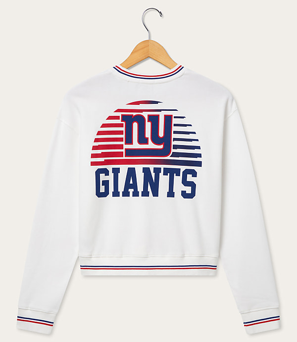 A white sweatshirt with a New York Giants logo on the back is hanging on a wooden hanger against a plain white background.
