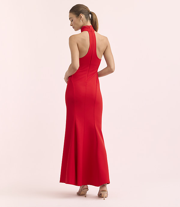 A woman in a red halter gown stands against a soft pink background.