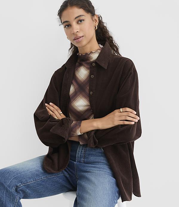 A woman in a brown corduroy shirt and jeans sits against a plain white background.