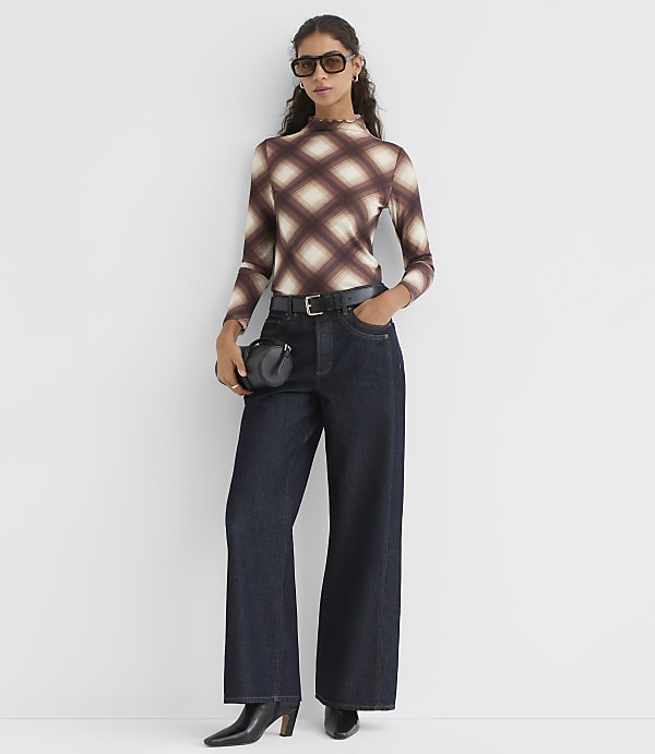 A woman in a diamond-patterned top and wide-leg jeans stands against a plain white background.