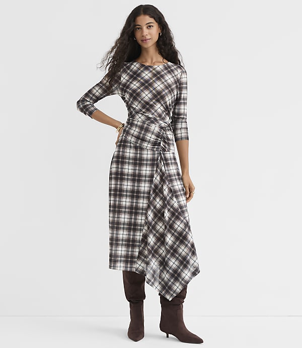 A woman in a plaid dress and boots stands against a plain white background.