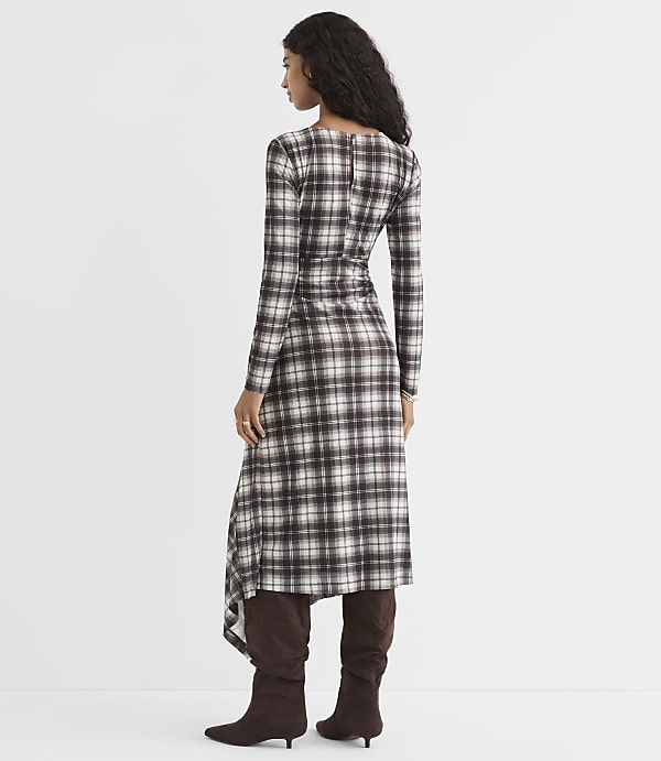 A woman in a plaid dress and brown boots stands against a plain white background.
