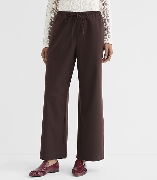 A person stands in brown wide-leg pants and red loafers against a plain white background.