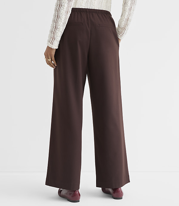 A person wearing brown wide-leg pants and a white lace top stands against a plain white background.