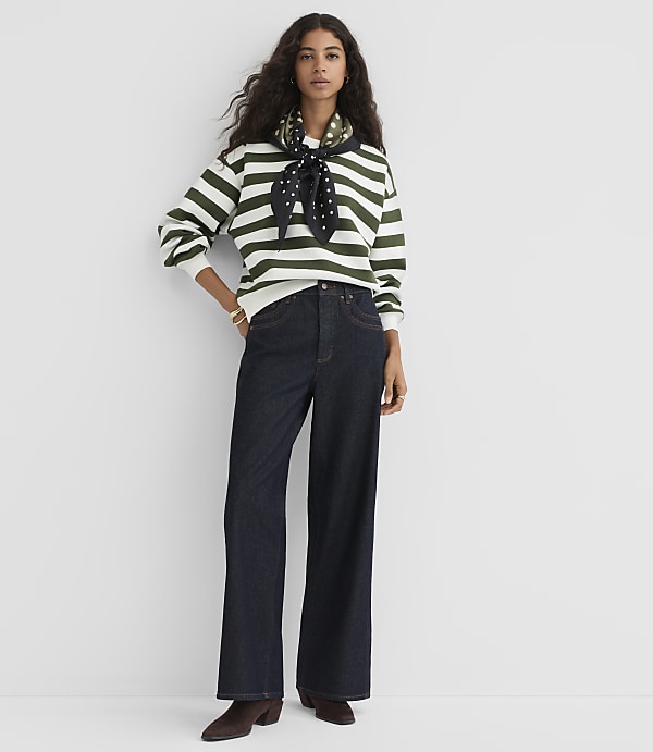 A woman in a striped sweater and wide-leg jeans stands against a plain white background.