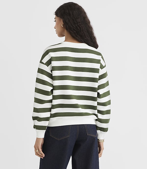 A woman in a green and white striped sweater and dark jeans stands against a plain white background.