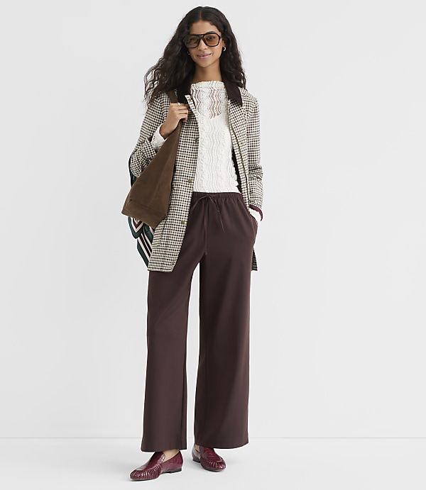 A woman in a patterned blazer and brown wide-leg pants stands against a plain white background.