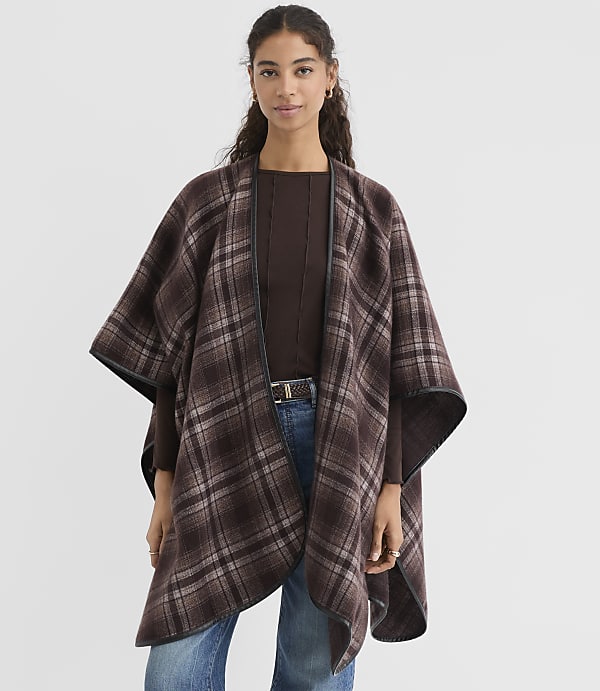 A woman in a brown plaid poncho stands against a plain white background.