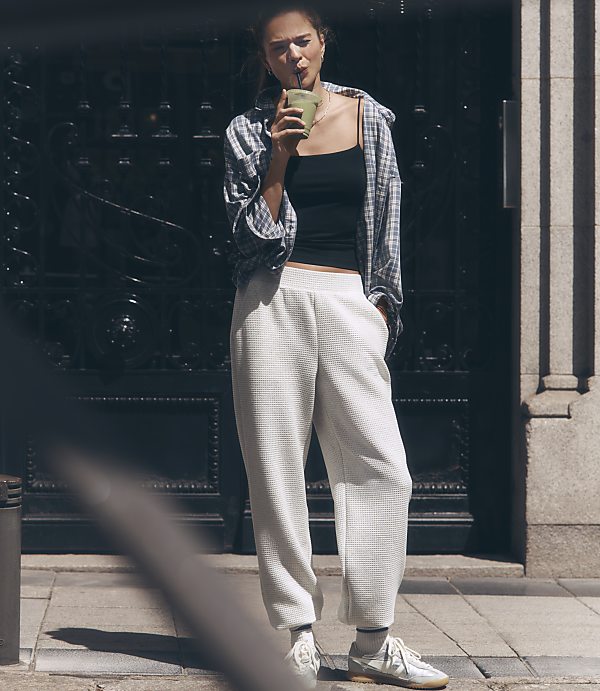 A woman in casual attire sips a green drink in front of a dark, ornate doorway.