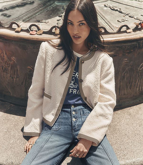 A woman in a tweed jacket and jeans sits in front of a decorative fountain with love locks.