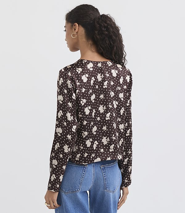 A woman in a floral print blouse and jeans stands against a plain white background.