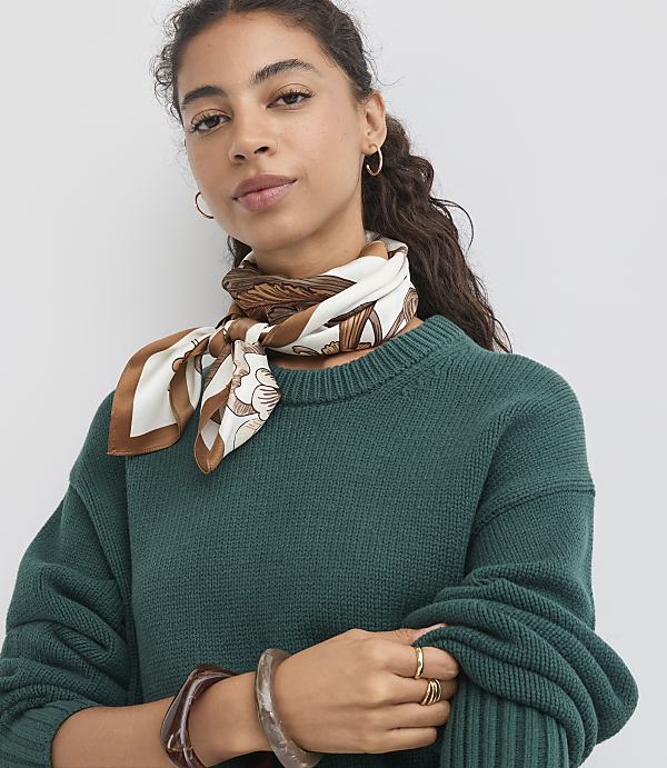 A woman with curly dark hair and a patterned silk scarf around her neck poses in front of a plain white background.