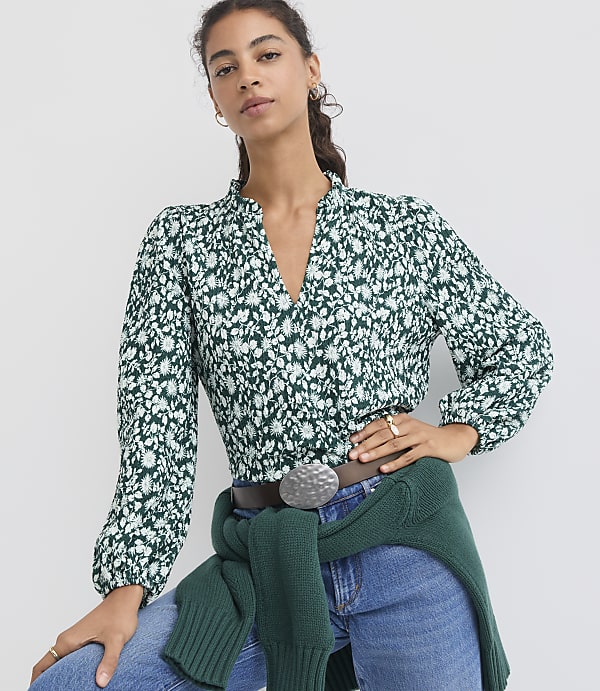 A woman in a floral blouse and jeans stands against a plain white background.