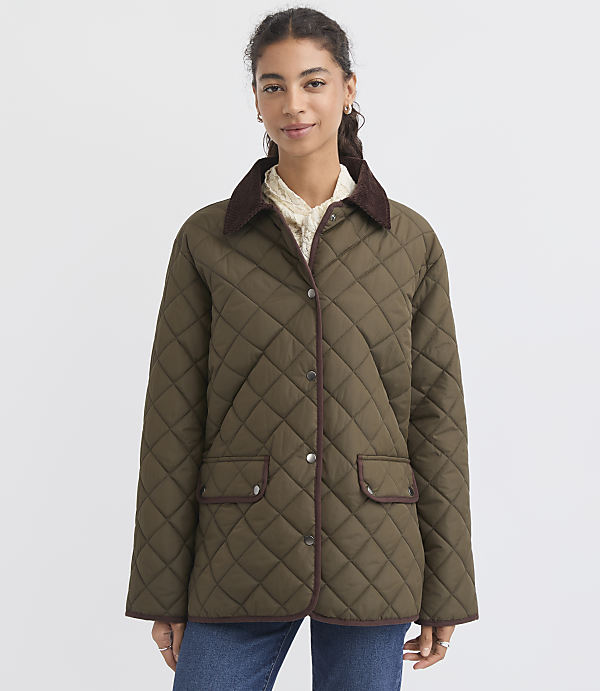A woman in a quilted olive green jacket with brown trim stands against a plain white background.