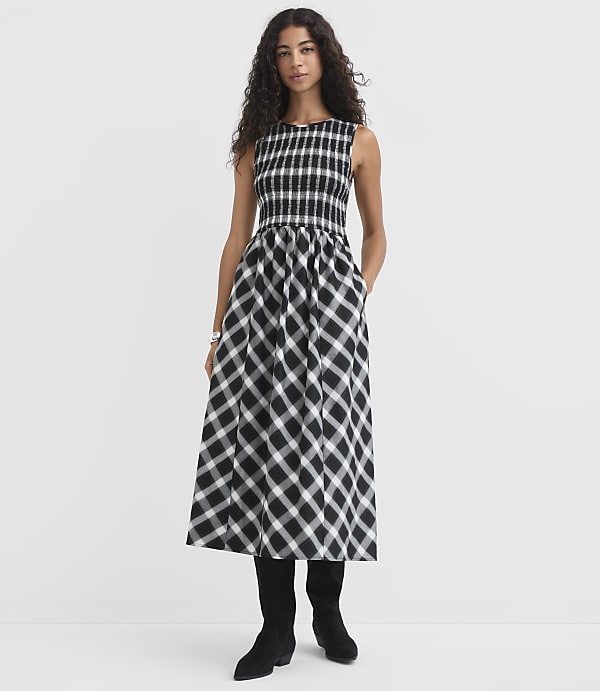 A woman in a black and white checkered dress stands against a plain white background.
