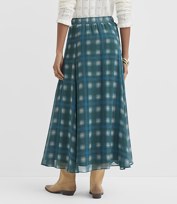 A person wearing a teal plaid maxi skirt and tan boots stands against a plain white background.