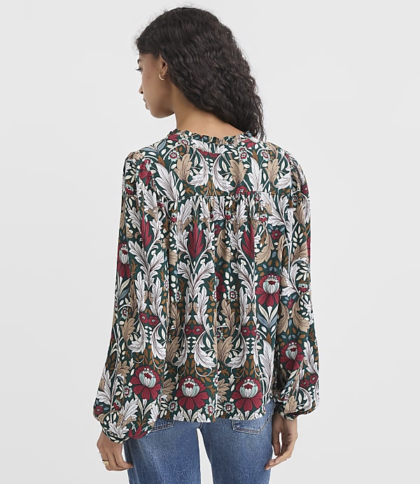 A woman in a patterned blouse stands against a plain white background.