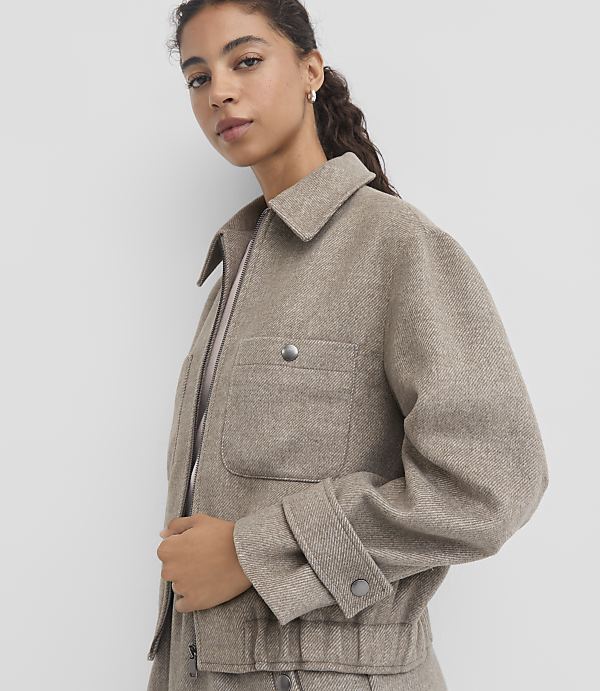 A woman in a textured beige jacket stands against a plain white background.