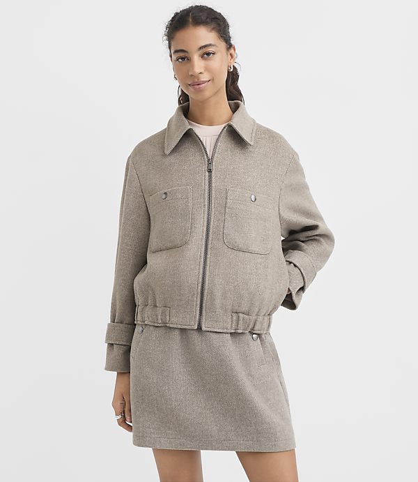 A woman in a beige jacket and skirt stands against a plain white background.