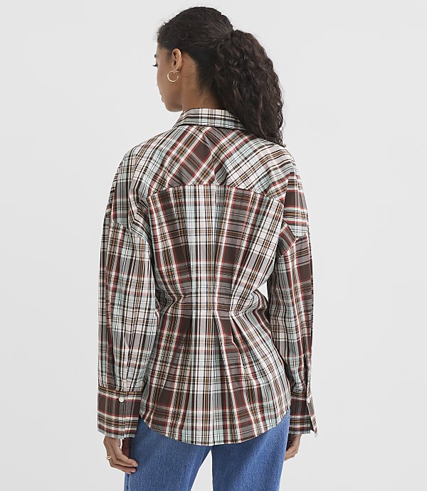 A woman in a brown plaid shirt stands against a plain white background.