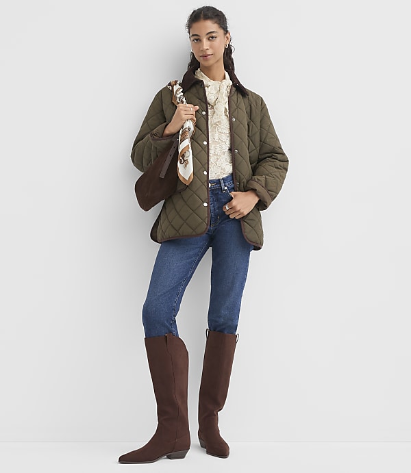 A woman in a quilted jacket, jeans, and boots stands against a plain white background.