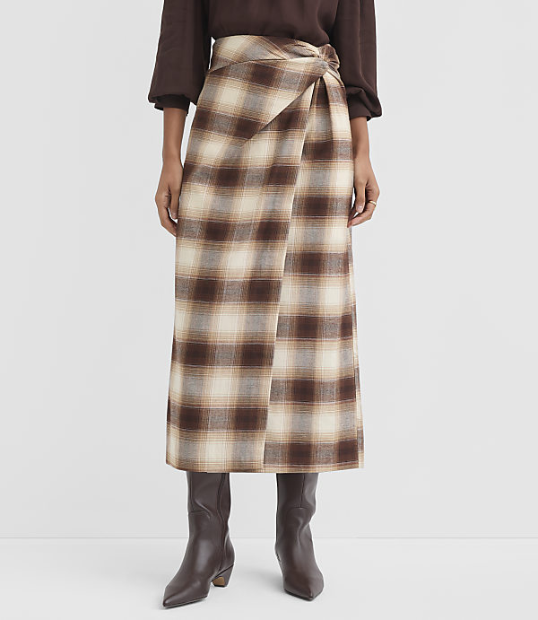 A person stands wearing a brown and cream plaid wrap skirt and dark brown boots against a plain white background.