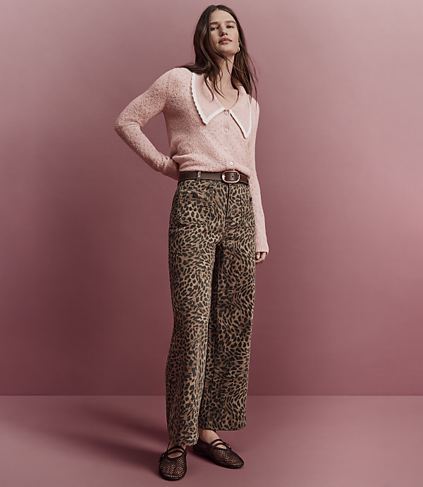A woman in a pink fuzzy sweater and leopard print pants stands against a solid pink background.