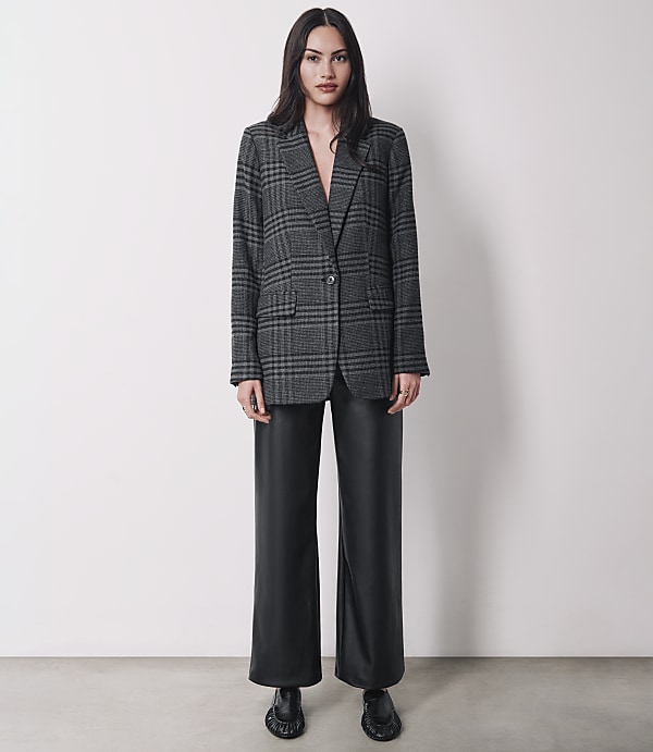 A woman in a plaid blazer and black leather pants stands against a plain white background.