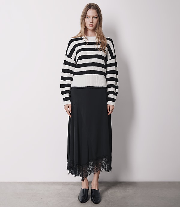 A woman in a striped sweater and black skirt stands against a plain white background.