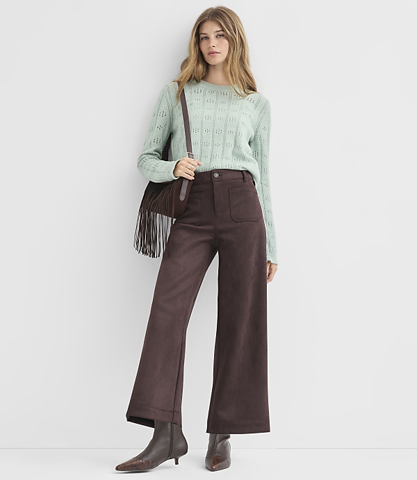 A woman in a light green sweater and brown wide-leg pants stands against a plain white background.