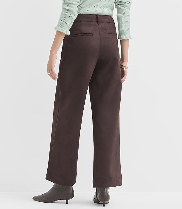 A person wearing brown wide-leg pants and a light green sweater stands against a plain white background.