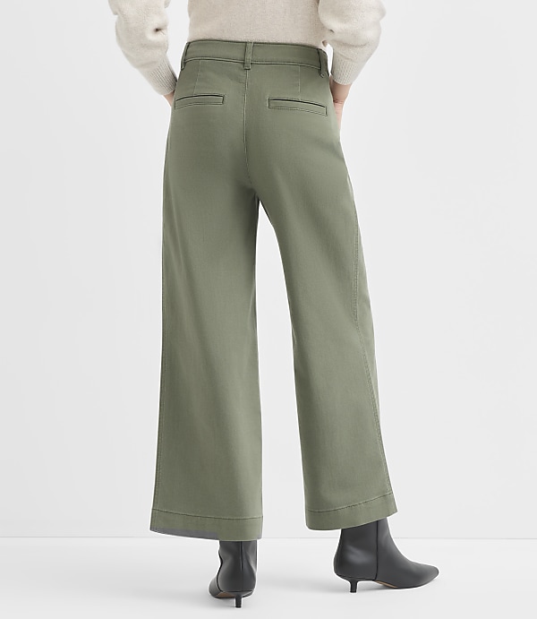 A person wearing olive green wide-leg pants and black boots stands against a plain white background.