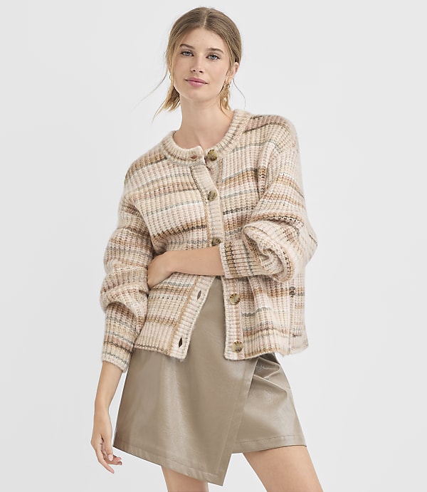 A young woman in a plaid cardigan and a leather skirt stands against a plain white background.