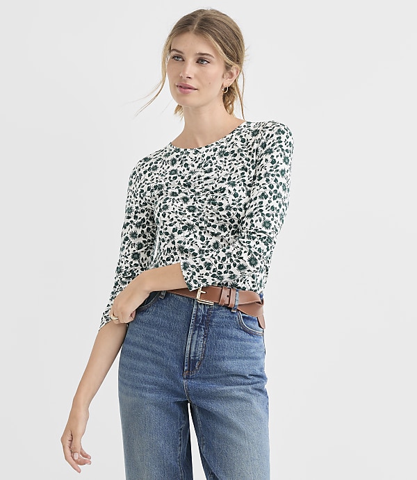 A woman in a floral top and jeans stands against a plain white background.