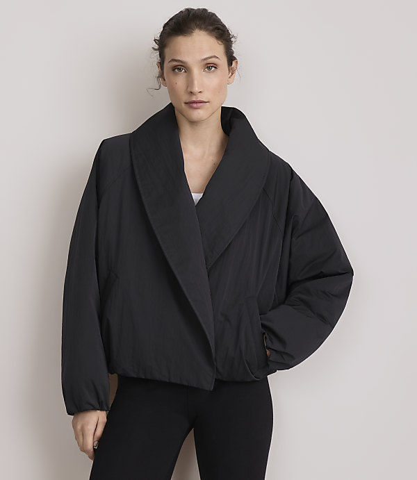 A woman in a black puffer jacket and leggings stands against a plain, light gray background.
