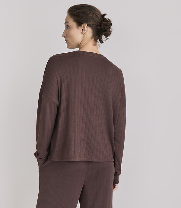 A woman in a brown ribbed top and pants stands with her back to the camera against a plain gray background.