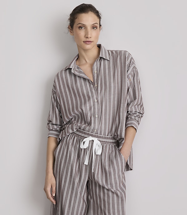 A woman in striped pajamas stands against a plain gray background.