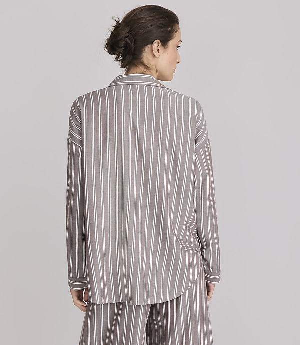 A woman in a striped pajama set stands against a plain gray background.