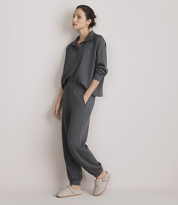 A woman in a grey loungewear set stands against a plain, light-colored wall.