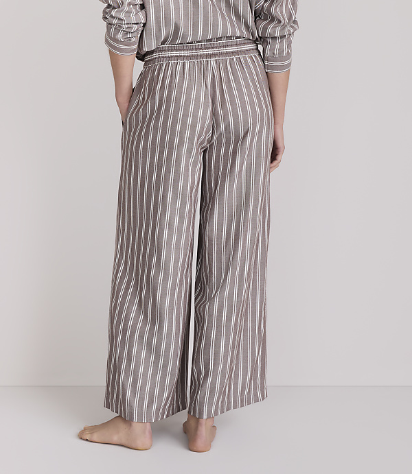 A person stands barefoot in striped pajama pants against a plain, light-colored background.