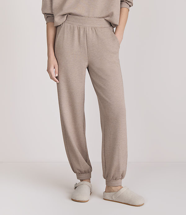 A person stands in beige loungewear and slippers against a plain white background.