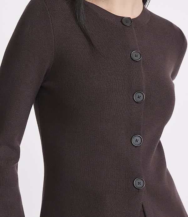 A close-up of a person wearing a dark brown, button-up cardigan with a plain background.
