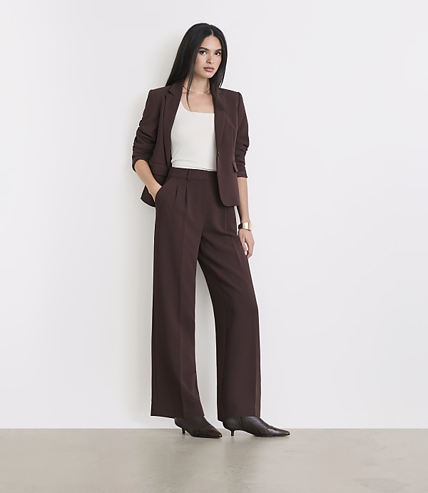 A woman in a brown suit stands against a plain white background.