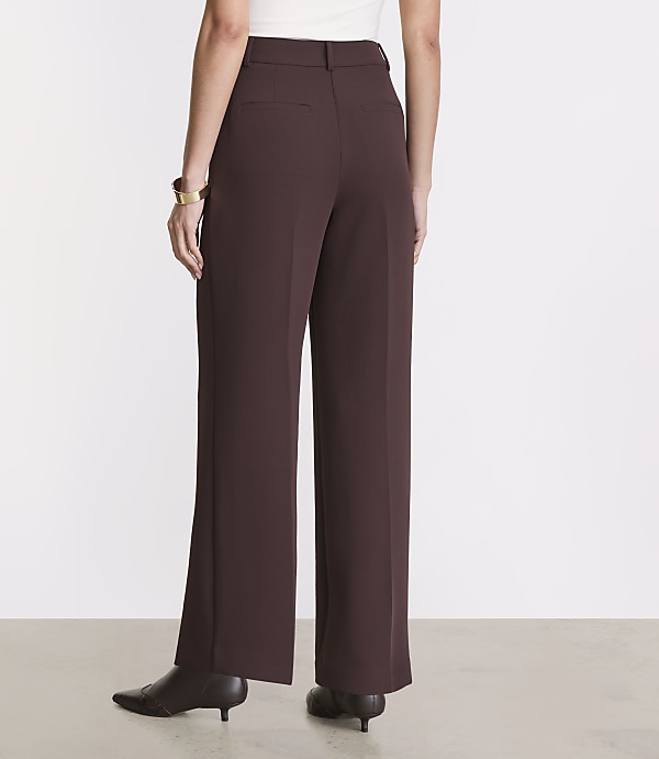 A person wearing brown wide-leg trousers and pointed-toe heels stands against a plain white background.