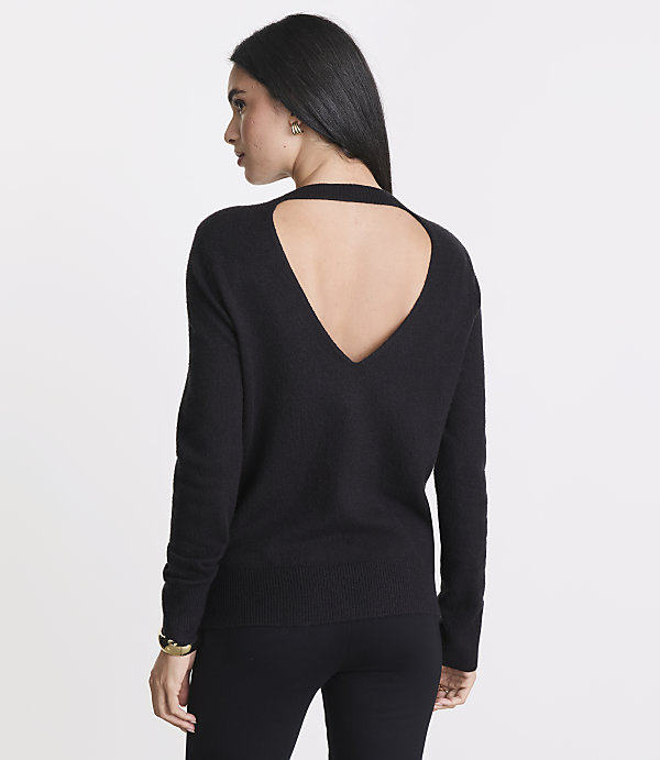 A woman in a black sweater with a cutout back stands against a plain white background.