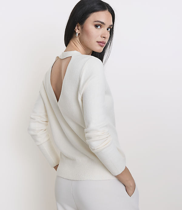 A woman in a cream sweater and pants stands against a plain white background.