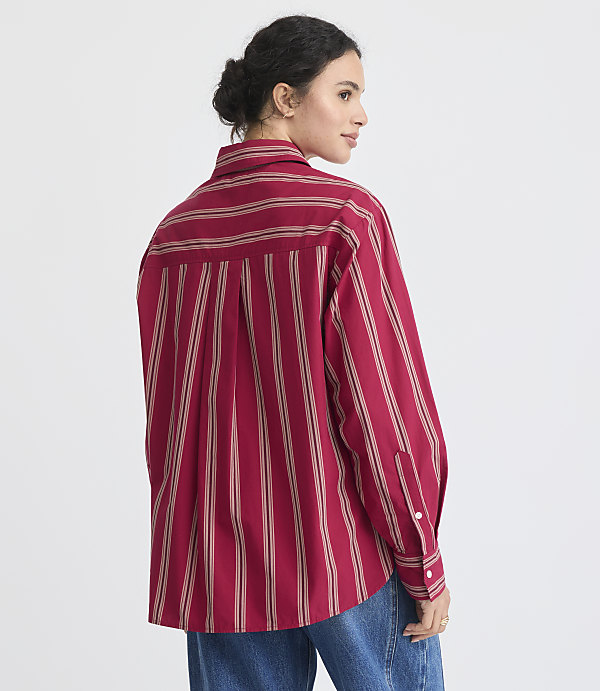 A woman in a red striped shirt and tan pleated skirt stands against a plain white background.