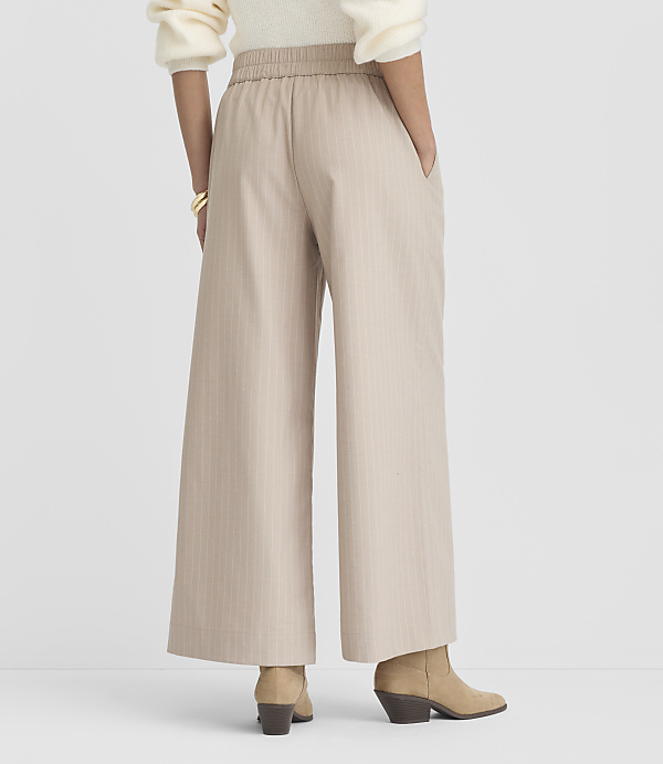 A person wearing beige pinstripe wide-leg pants and tan boots stands against a plain white background.