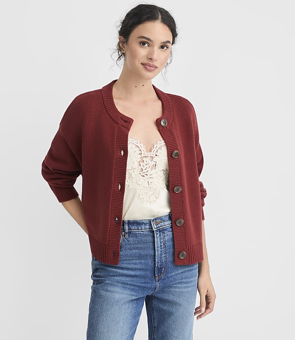 A woman in a rust-colored cardigan and lace camisole stands against a plain white background.